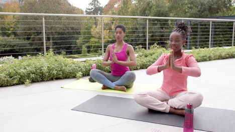 happy african american daughter and mother practicing yoga in sunny garden, slow motion