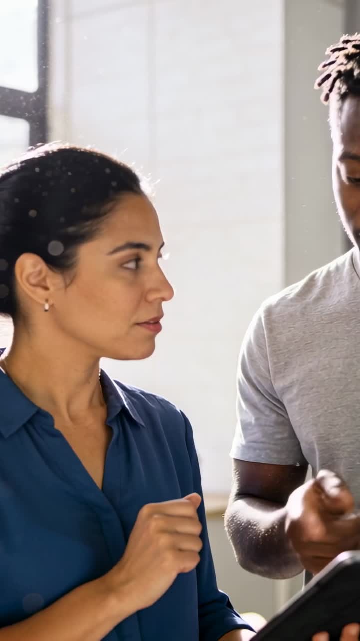 Vertical video: Woman pointing, man holding tablet, both leaning and tapping, reviewing project