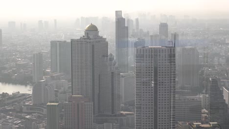 hand-held shot of large skyscrapers under smog in downtown bangkok