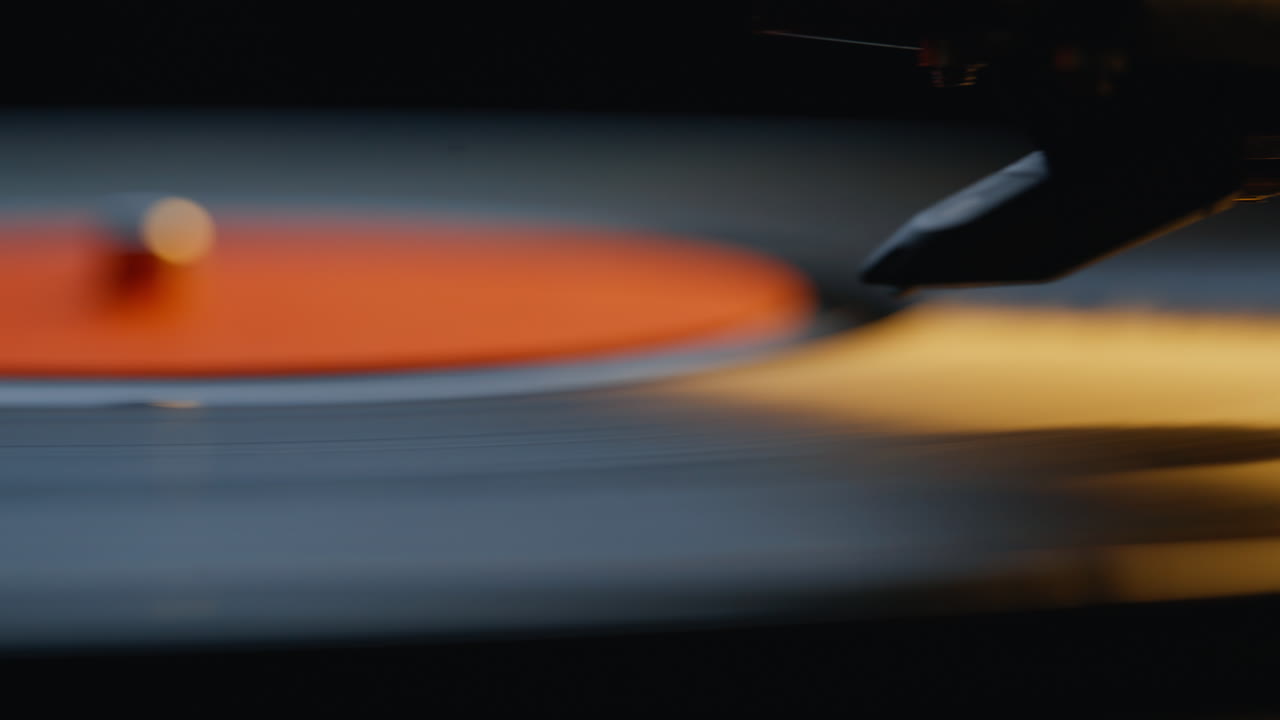 Macro needle touching grooves on vinyl record player performing song. Black disc