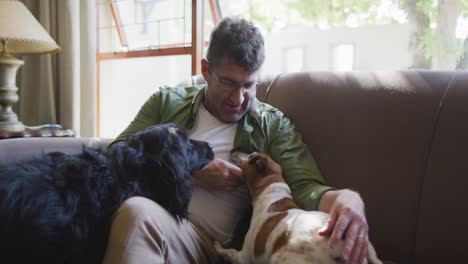 hombre caucásico sentado en el sofá, acariciando perros, sonriendo en casa
