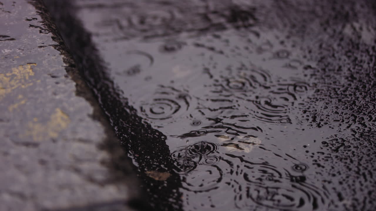 Close up footage of water on the street with raindrops falling into it in super slow motion
