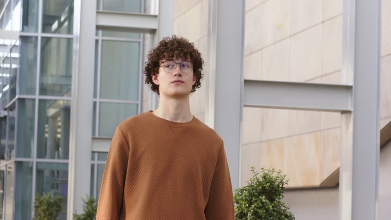 Ein männlicher Student, der neben einem Gebäude geht und auf einen roten Ordner blickt, wirft einen Blick nach oben und studiert die Architektur