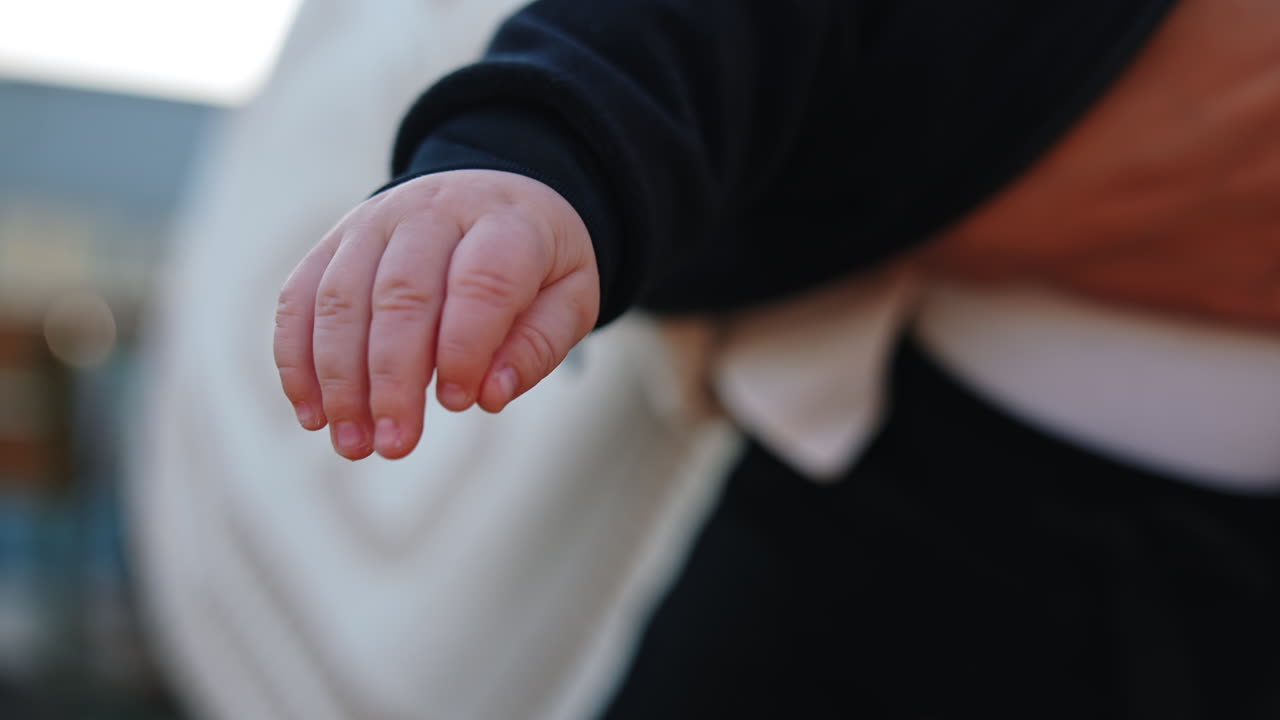 Hands of a little baby wearing black sweater. Close up. Child in mom's hands close up.