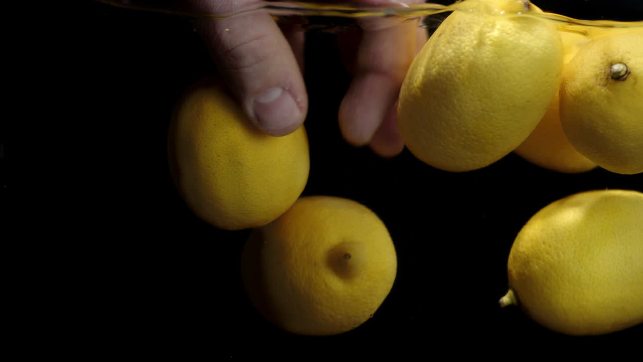 la mano de un hombre bajo el agua con limones frescos.