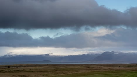 time lapse shot of flying clouds at sky over iceland landscape and snowy mountains in background