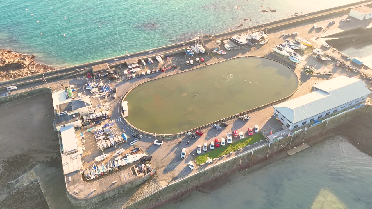 Guernsey St Peter Port.Dropping overhead drone footage of model yacht pond on bright sunny afternoon with clear blue sea,Guernsey Yacht Club and boats on hardstanding