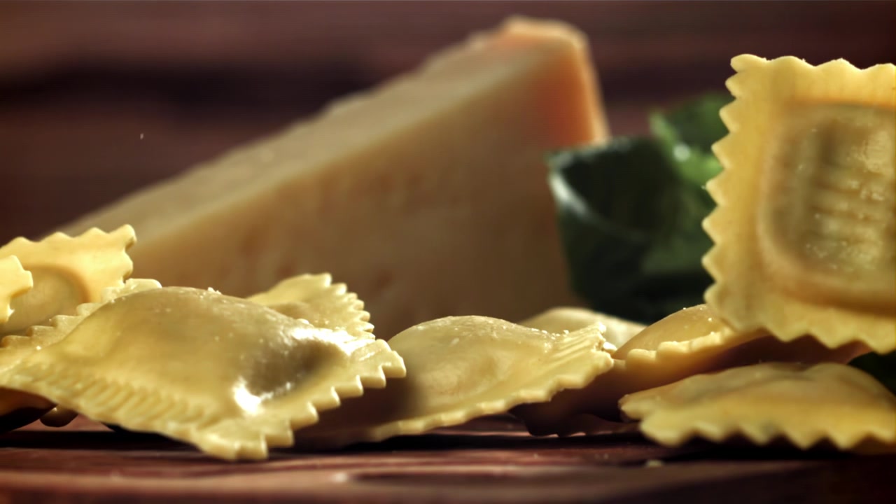 Ravioli freschi che cadono al rallentatore su una superficie di legno con Parmigiano e basilico