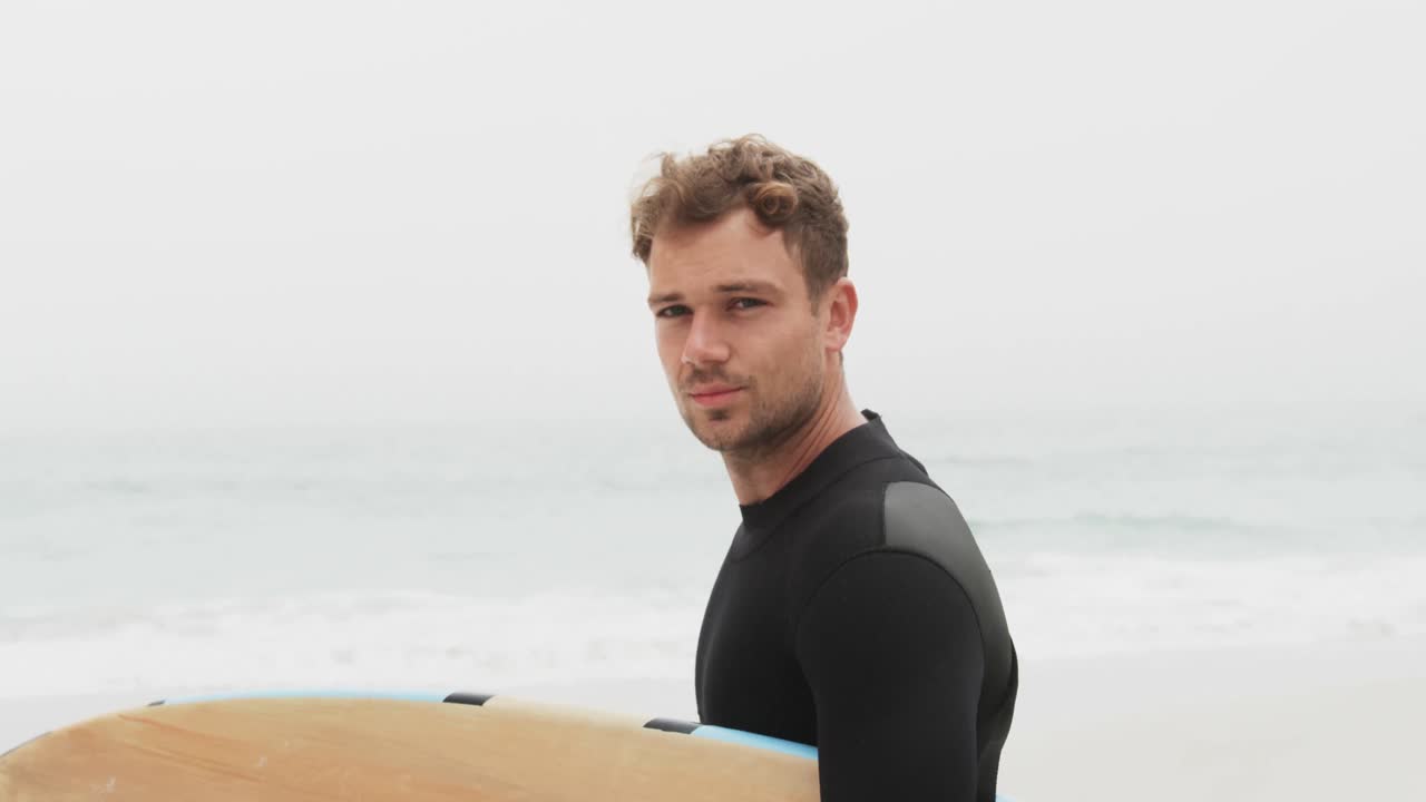 해변 4k에 서핑 보드와 함께 서 있는 남성 서퍼의 측면 뷰