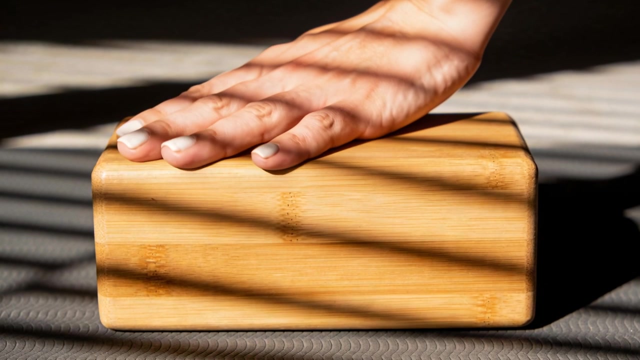 Main aux ongles blancs s'approchant, pressant et glissant sur un bloc de bois posé sur un tapis, effectuant des tests sous les stores.