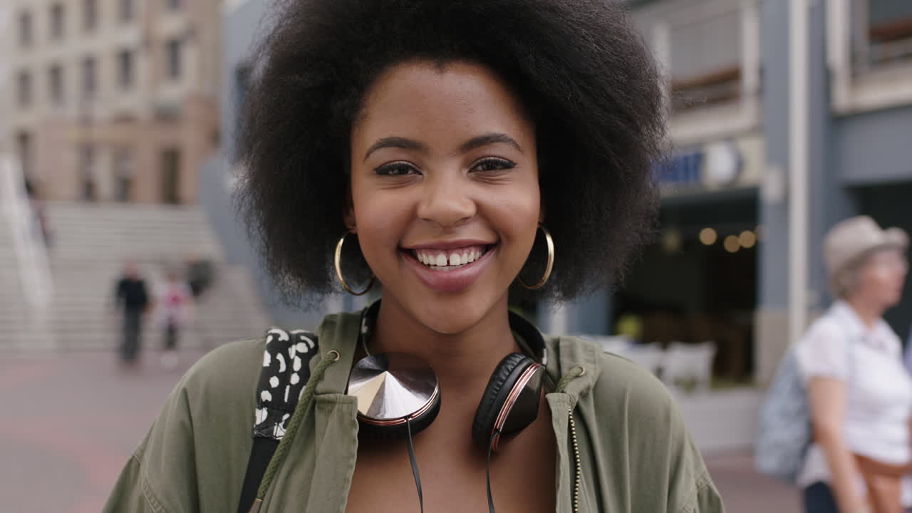 retrato en cámara lenta de una joven mujer afroamericana de moda con cabello afro rizado sonriendo feliz al aire libre urbano