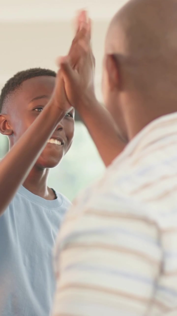 Vertical video: Speaking youth causing adult to reach for high five at home by window, in blue tee