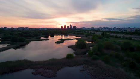 Aerial-View-Over-Vacaresti-Delta-At-Sunset-With-Birds-Flying,-Cityscape-In-The-Background,-Sunset-Colors,-Orange,-Red,-Yellow,-Bucharest,-Romania