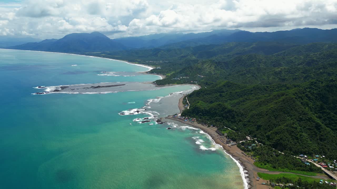 A birds-eye view of Dingalan, Aurora, Philippines, showcasing turquoise waters, sandy shoreline, and lush green mountains blending into the dramatic coastal landscape