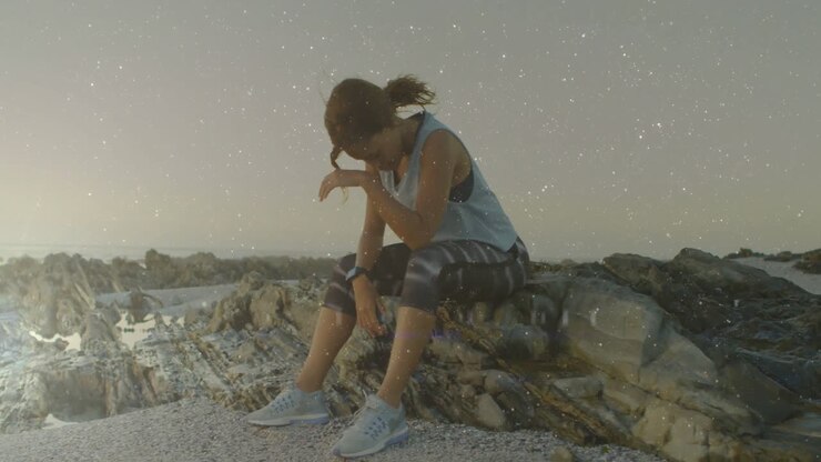 Sportlerin blickt bei Sonnenaufgang auf felsige Küste und sinkt erschöpft mit animierter Fitnessanzeige zusammen