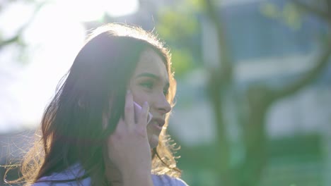 primer plano de una mujer caucásica en el parque hablando por teléfono, sonriendo