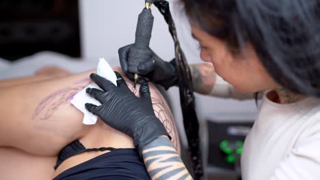 tattooist applying tattoo on hip of anonymous woman in shop