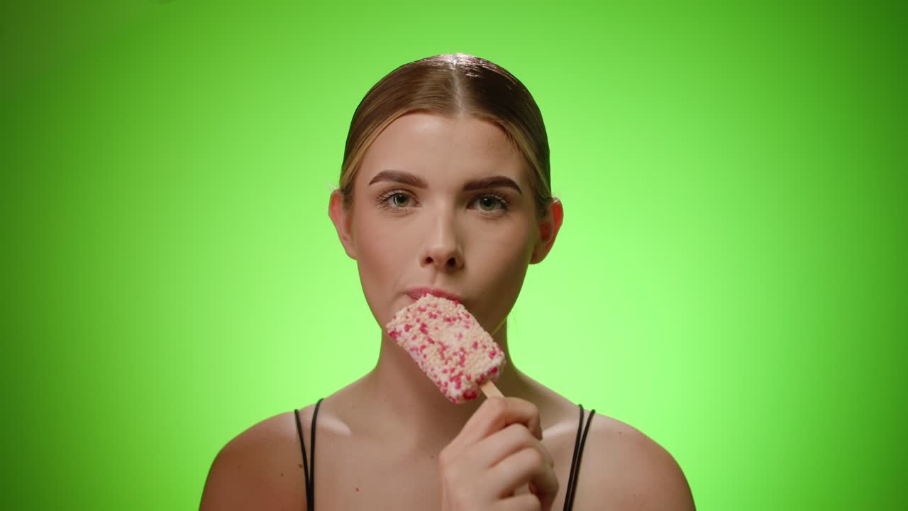 mujer caucásica toma un bocado delicioso blanco, helado de bayas, fondo verde
