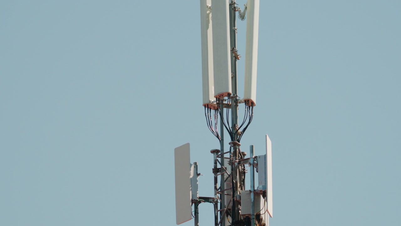 Close up of a telecommunications antenna mounted on a metal tower structure against a clear blue sky