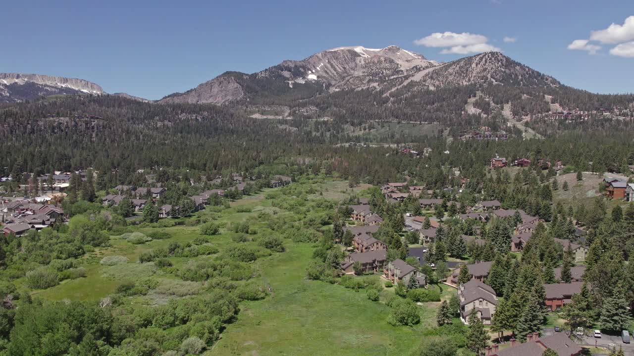 4k drone footage camera pan right of beautiful Mammoth Mountain in the summertime with a view of a lush green meadow and cabins