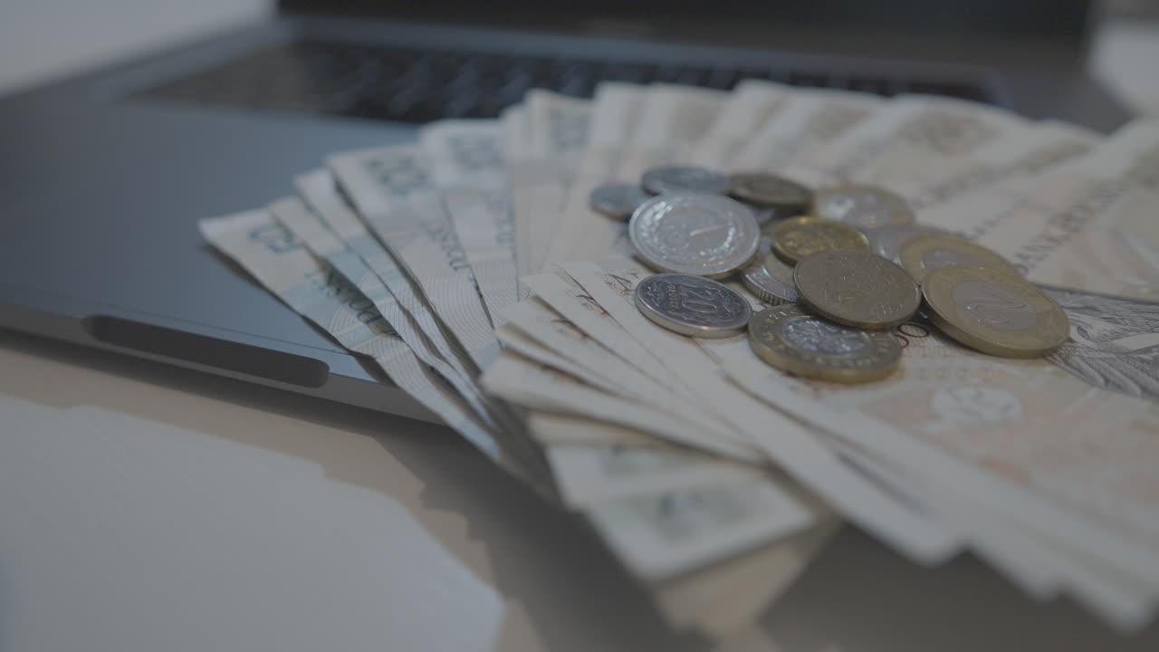 Close Up View Of Various Polish Bank Notes Fanned Out With Coins Stacked On Top Resting On Laptop