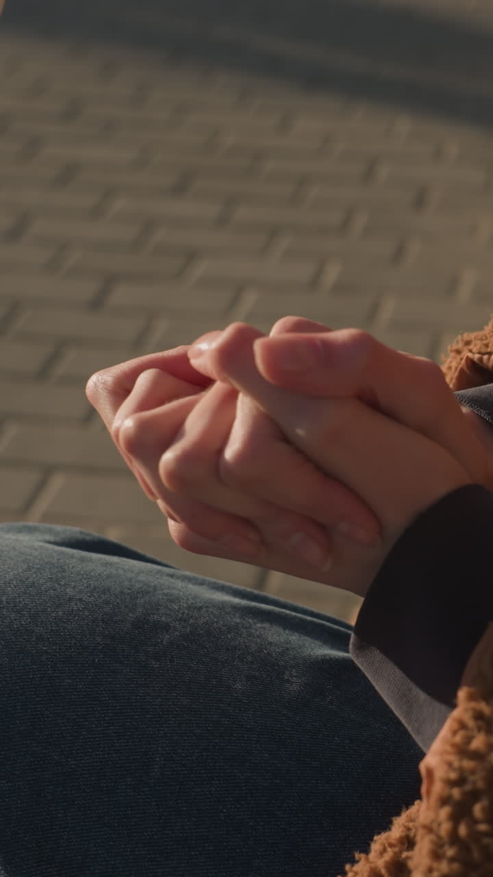 primer plano de una persona sentada con la cara no visible, con pantalones vaqueros azules y un abrigo marrón, doblando y frotando las manos juntas. las manos en un gesto de ansiedad o pensamiento profundo