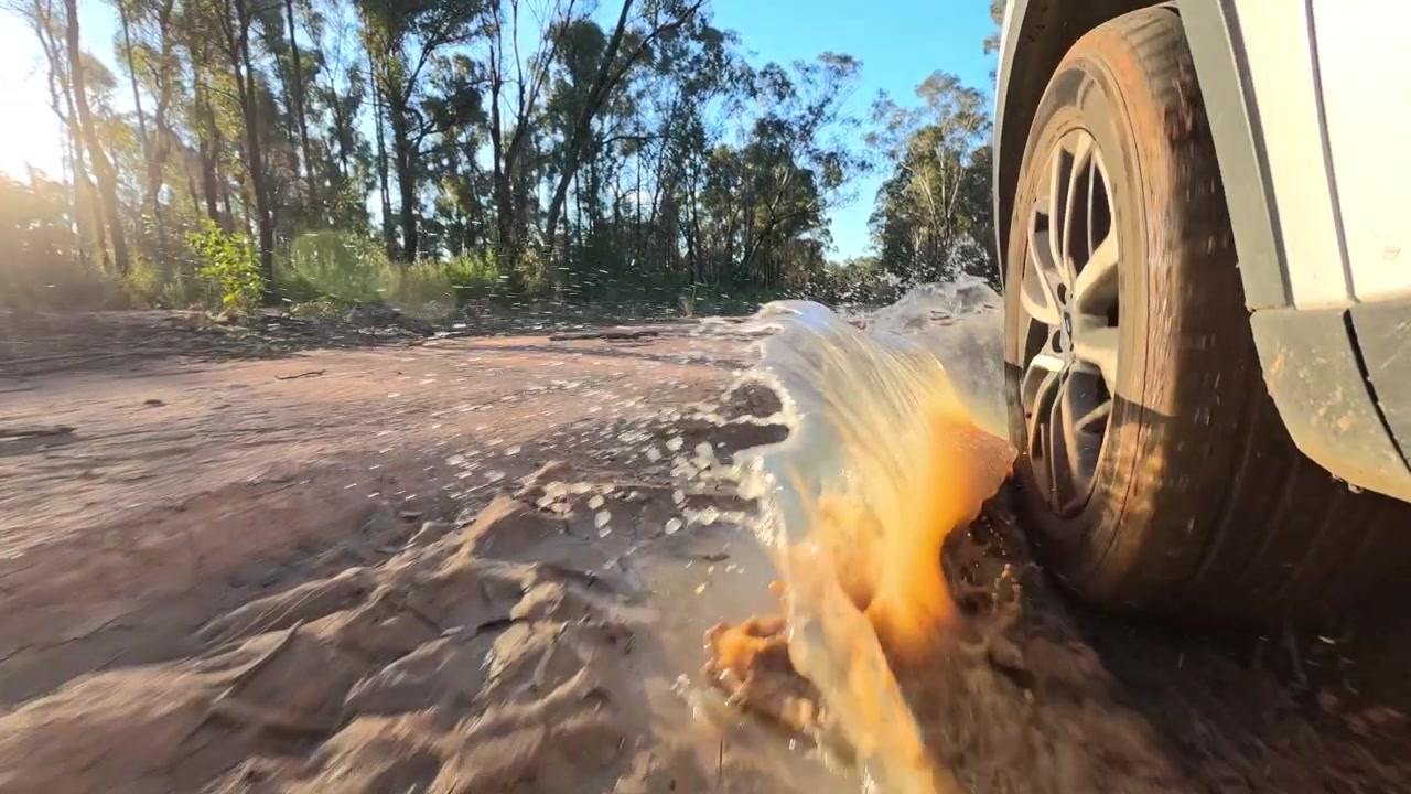 Low angle view of a vehicle tire driving through muddy puddle water on rural road.