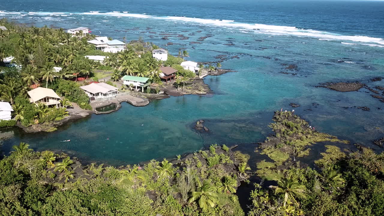 Aerial shot of a small tropical cove. Seaside houses around a clear blue lagoon.