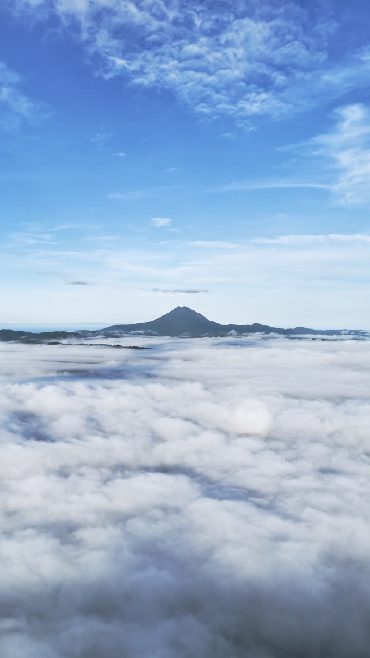 Portrait high-altitude panning drone shot above Malampaya Sound during a foggy morning, showing clouds below, Mount Capoas on the horizon, and a clear blue sky