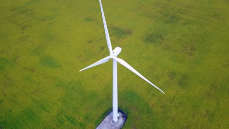Aerial-Birdseye-view-orbiting-spinning-wind-turbine-generator-on-green-idyllic-farmland