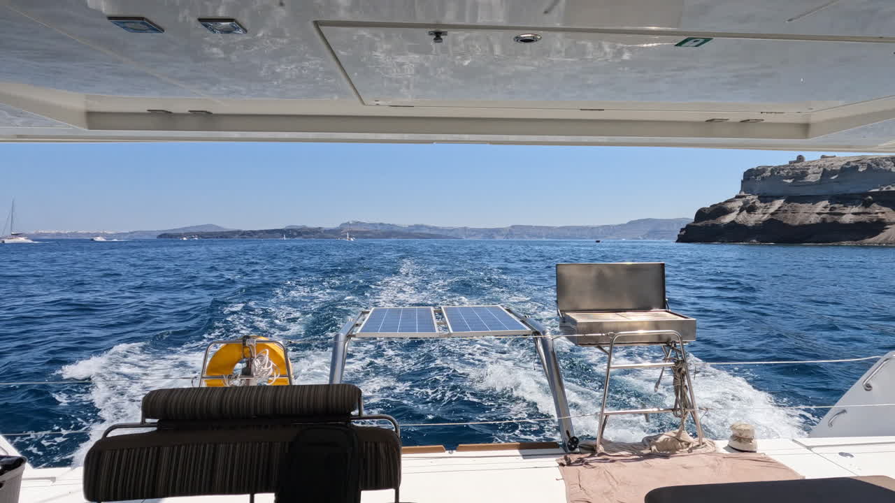 pov mirando desde la popa de un yate navegando más allá de la isla de thera santorini en grecia en un día de verano
