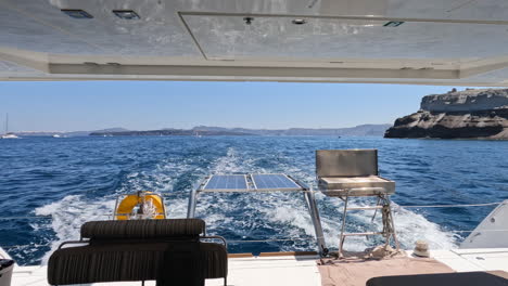 POV-looking-out-the-back-stern-of-a-yacht-sailing-past-the-island-of-Thera-Santorini-in-Greece-on-a-summers-day