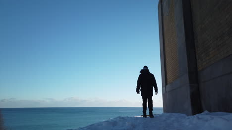 wide shot of a parka clad man arriving at a hilltop vista overlooking lake ontario