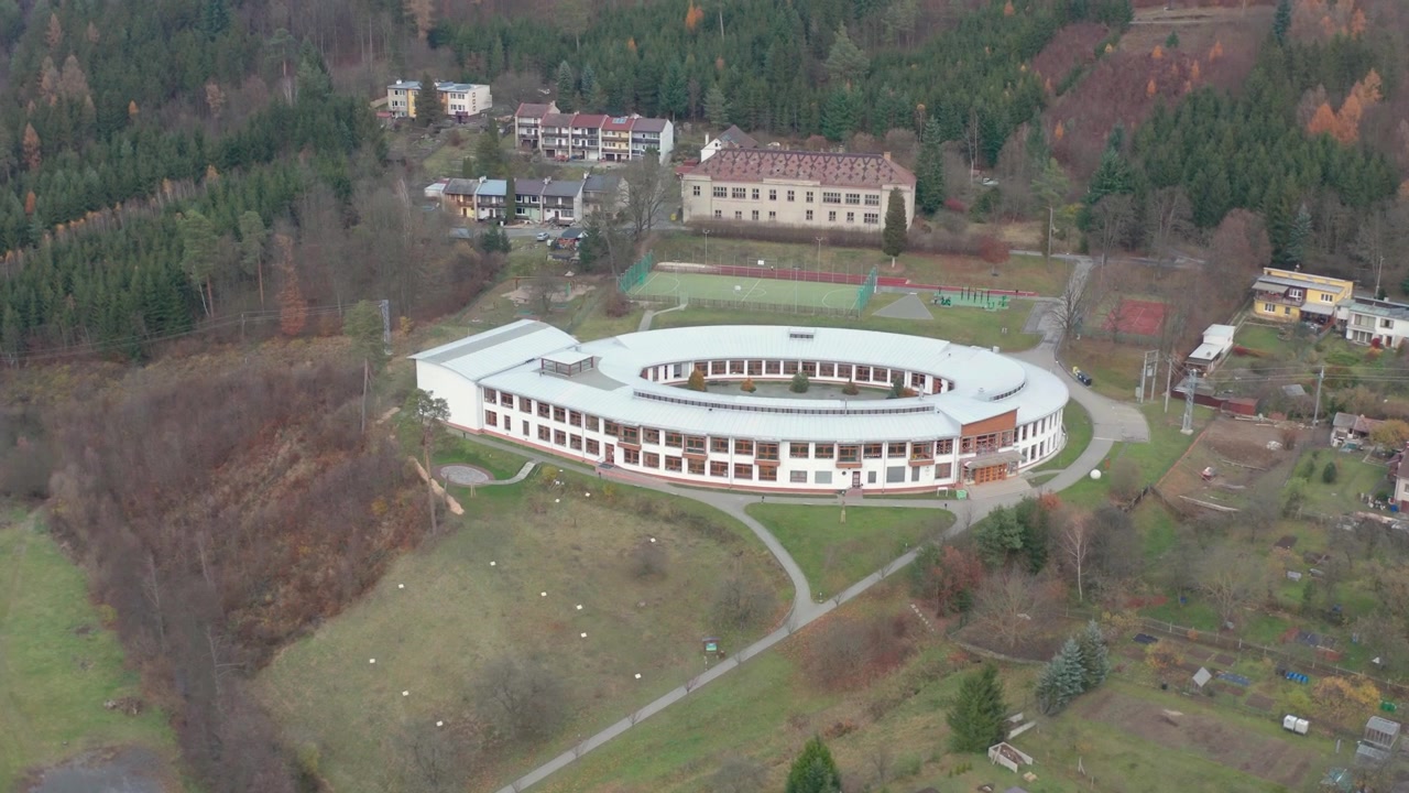 Dron latający wokół głównej szkoły w małym miasteczku Křtiny, aż do lasu i domów, pokazujący nowoczesny budynek szkoły