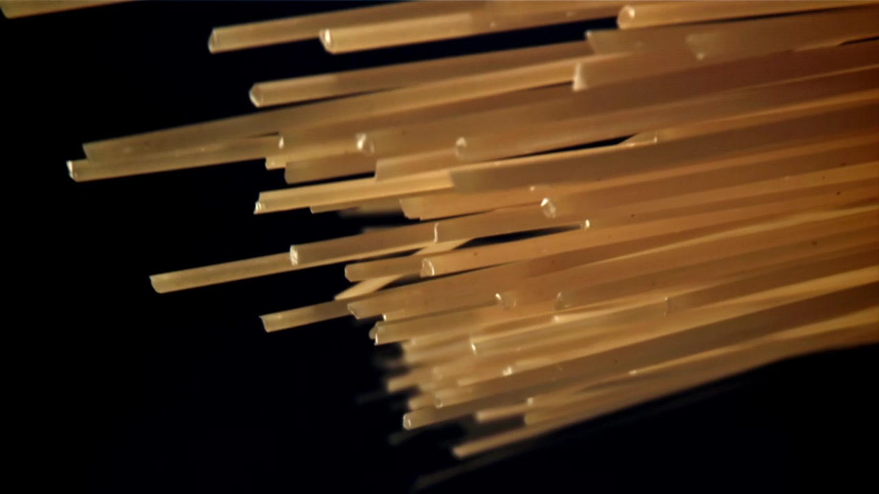 Spaghetti secchi che cadono contro uno sfondo nero