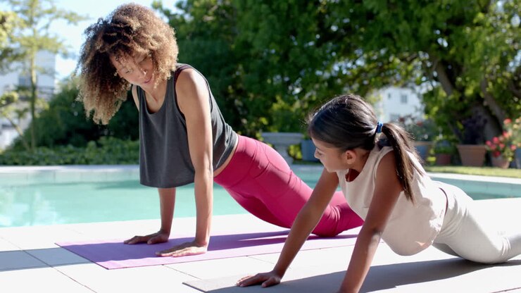 Happy biracial mother and daughter practicing yoga pose in sunny garden, slow motion