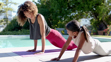 happy biracial mother and daughter practicing yoga pose in sunny garden, slow motion