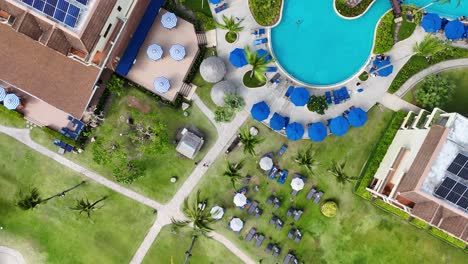 drone footage captures a vibrant resort pool in phuket, thailand, showcasing lush greenery, blue umbrellas, and solar-paneled roofs