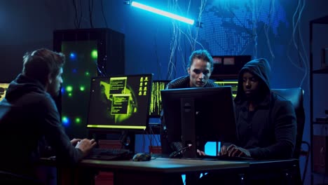 man in a hood and young woman working together and hacking programs in a dark room while other hacker or programs developer working alone