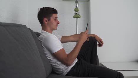 un joven feliz usa un teléfono inteligente mientras se sienta en un sofá
