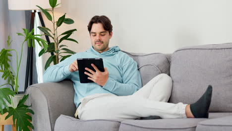 hombre, escribir y relajarse con la tableta en el sofá para ver