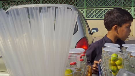 small child running a roadside cart selling fresh lemon soda to passersby in a bustling public marketplace.