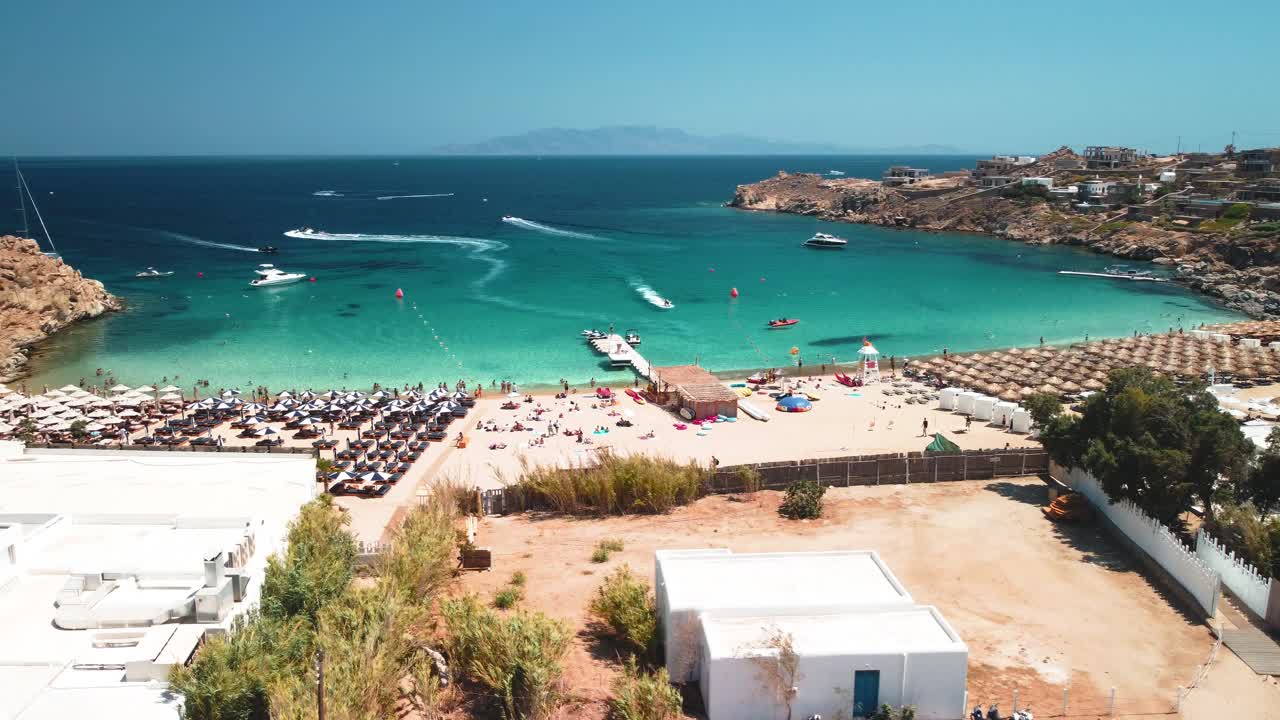 órbita aérea de drones filmada con la playa súper paraíso en mykonos, grecia durante un día soleado de cielo limpio con turistas y residentes de deportes acuáticos en la colina