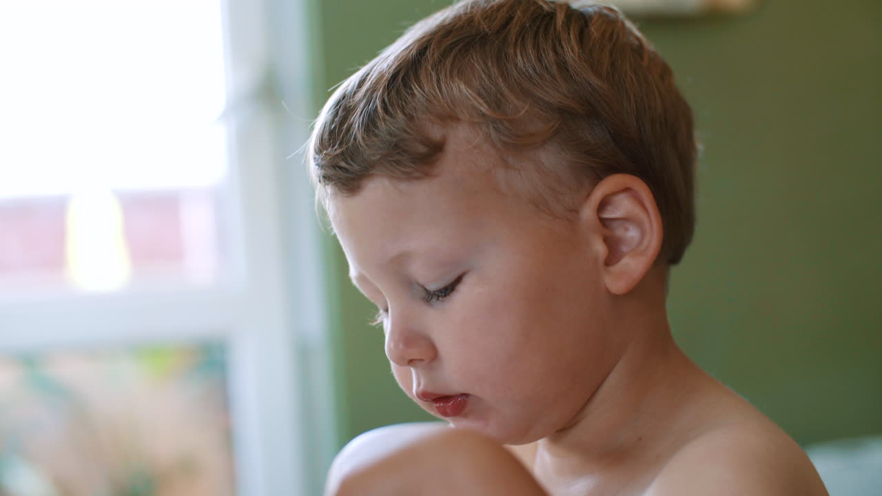 A white, blond and blue-eyed child boy who eats food with a spoon and looks away