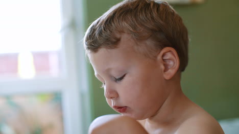 a white, blond and blue-eyed child boy who eats food with a spoon and looks away