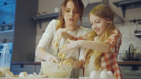 little blonde girl having fun while helping her mother to bake and make a daugh at the kitchen table in the evening. portrait shot. indoor