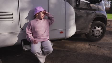 portrait of a girl in a pink hat sitting on the steps of a caravan, exposing her face to the sun