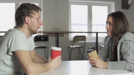 two friends are sitting at the table in cafe, drinking coffee-to-go in paper cups and talking. shot in 4k