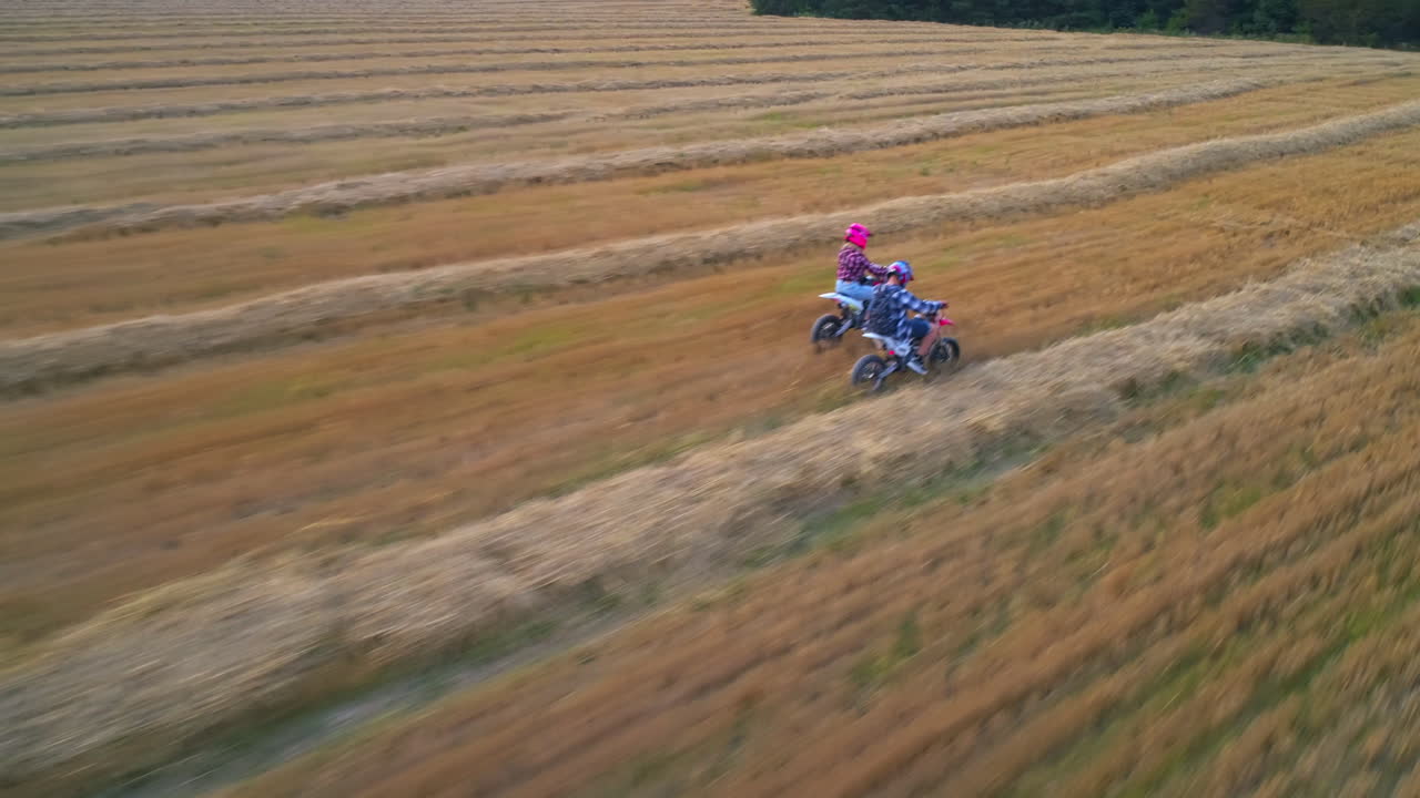 Giovane coppia in moto vicini l'uno all'altra. Persone che si divertono nel campo con erba tagliata al tramonto. Vista dall'alto