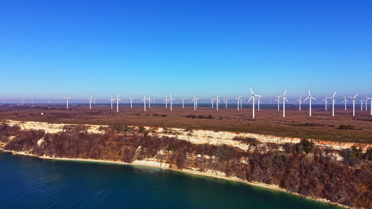 View of wind turbines along a coastline under a clear blue sky during the day near a flat landscape